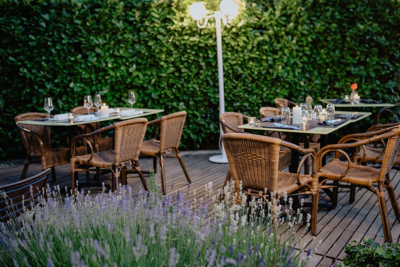 Cozy outdoor restaurant terrace with wicker chairs, tables, and lush green hedges.