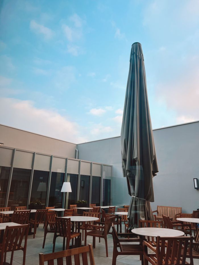 Peaceful outdoor patio with empty seating and a closed umbrella under a clear blue sky.